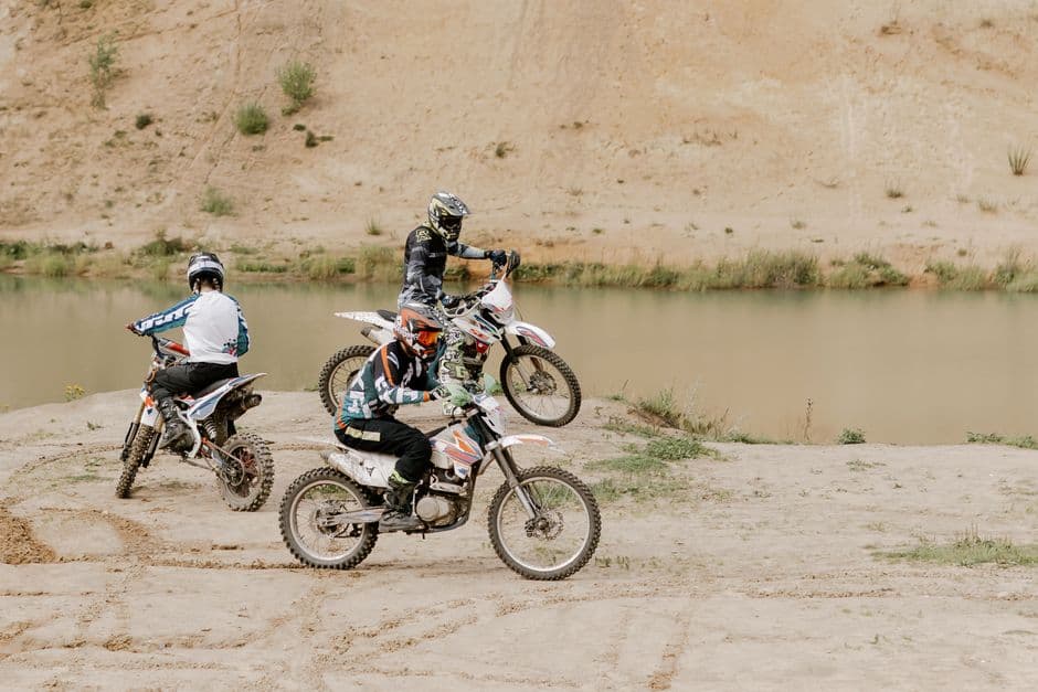 Three motocross riders enjoying an exciting off-road adventure near a serene lake.