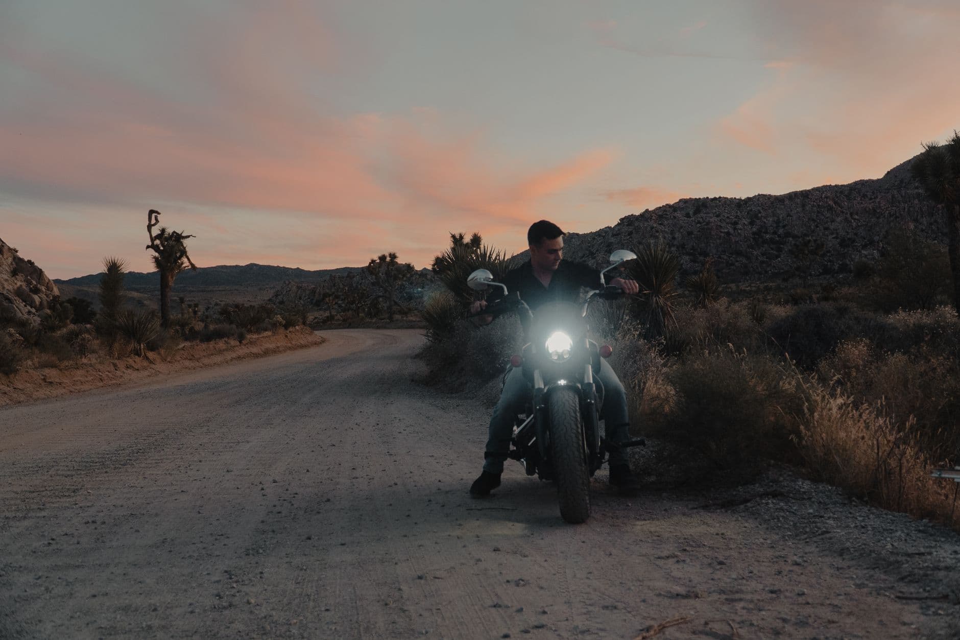 A lone biker on a motorcycle rides along a desert road during a striking sunset.