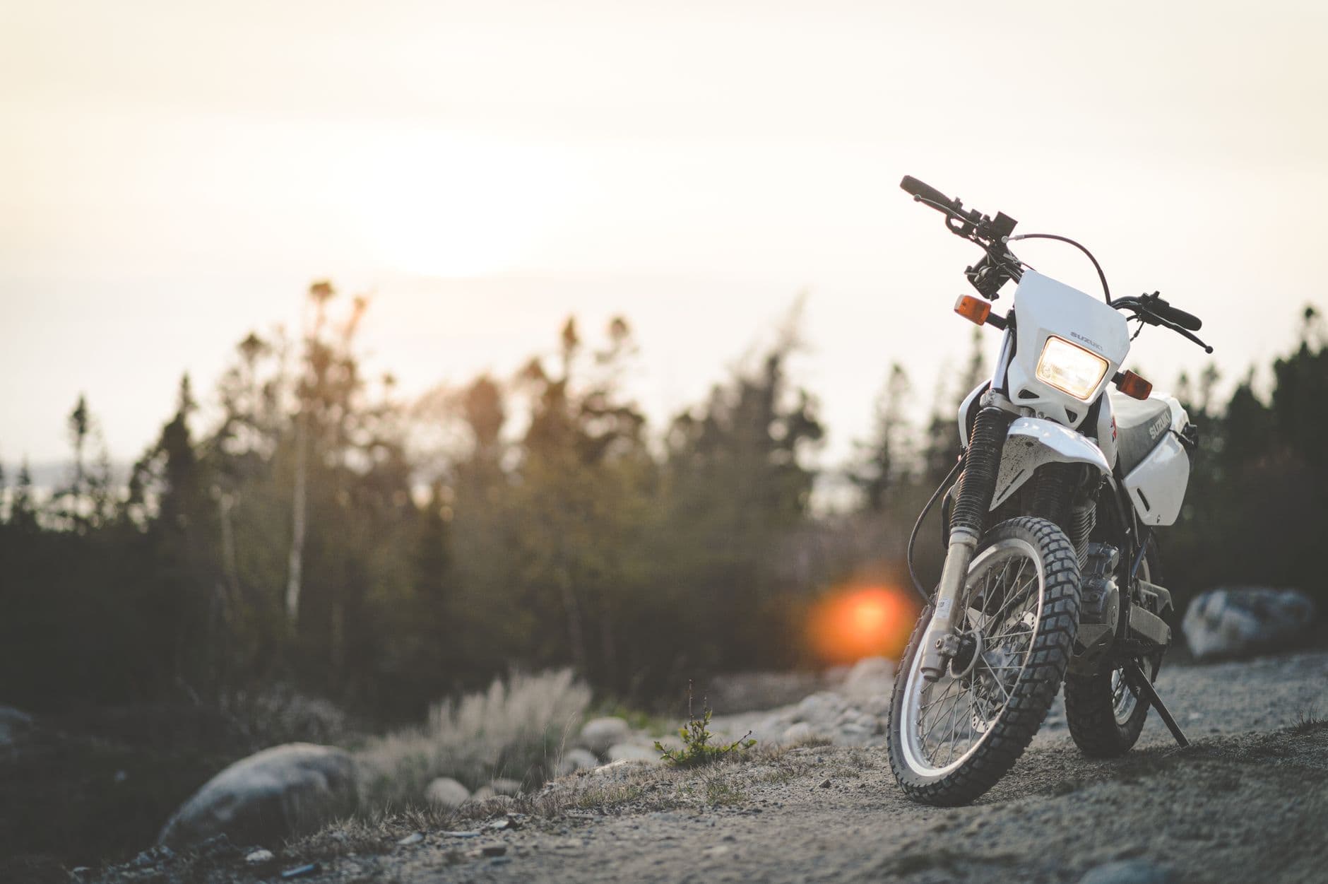 A parked motorbike on a gravel trail with a sunset background, evoking adventure and exploration.