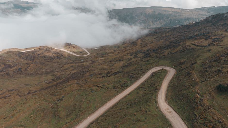 A winding dirt road through a misty mountain landscape with clouds hugging the peaks.